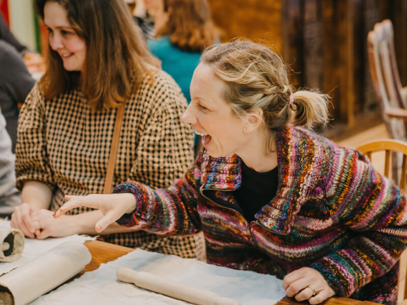 A woman laughs with a friend of screen at a pottery class.